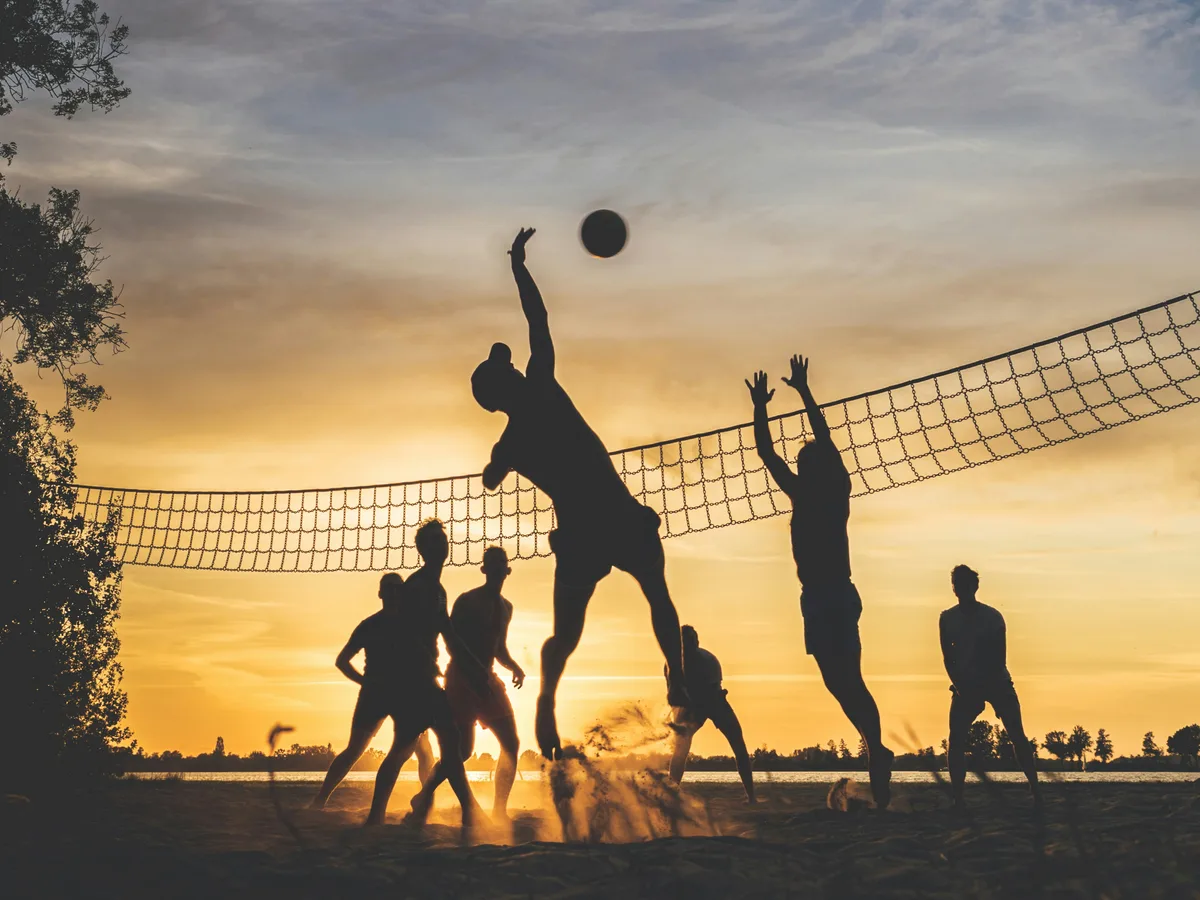 Friends playing volleyball together at sunset